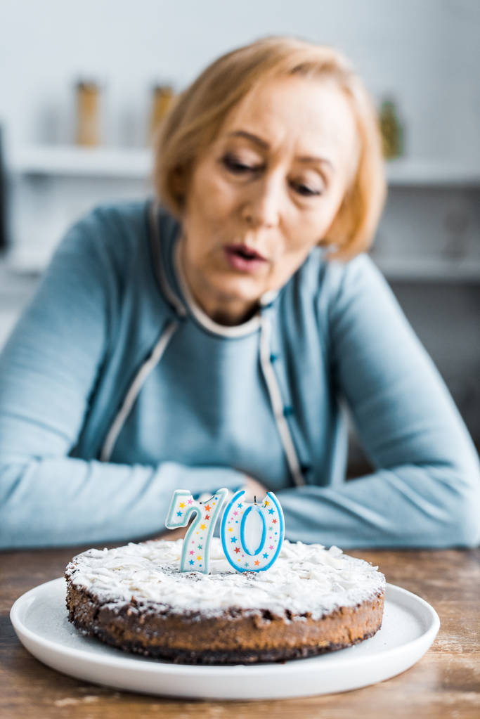 Selektywny fokus ciasto z '70' Zaloguj się na górze i starszy kobieta na tle podczas obchody urodzin - Zdjęcie, obraz