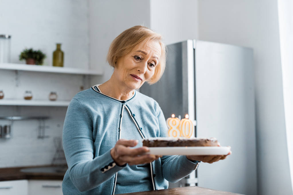 samotny senior kobieta trzyma tort z '80' znak na górze podczas obchody urodzin - Zdjęcie, obraz