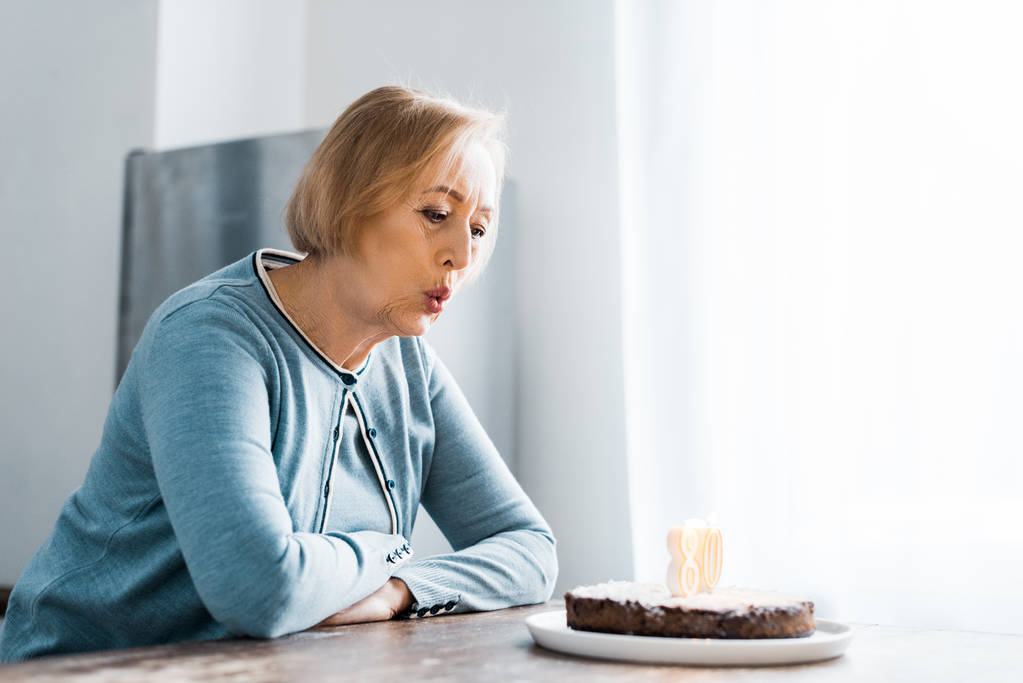 Seniorin bläst bei Geburtstagsfeier Kerzen auf Kuchen mit '80' -Schild aus - Foto, Bild