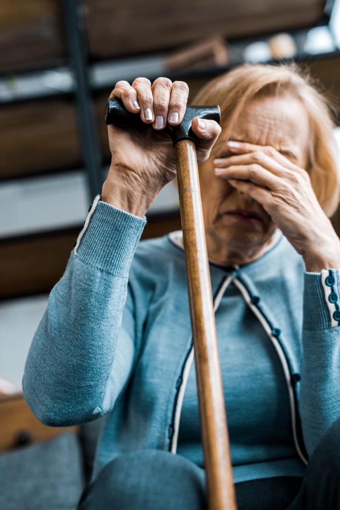 bouleversé femme âgée tenant bâton de marche, couvrant le visage avec la main et pleurant à la maison
 - Photo, image