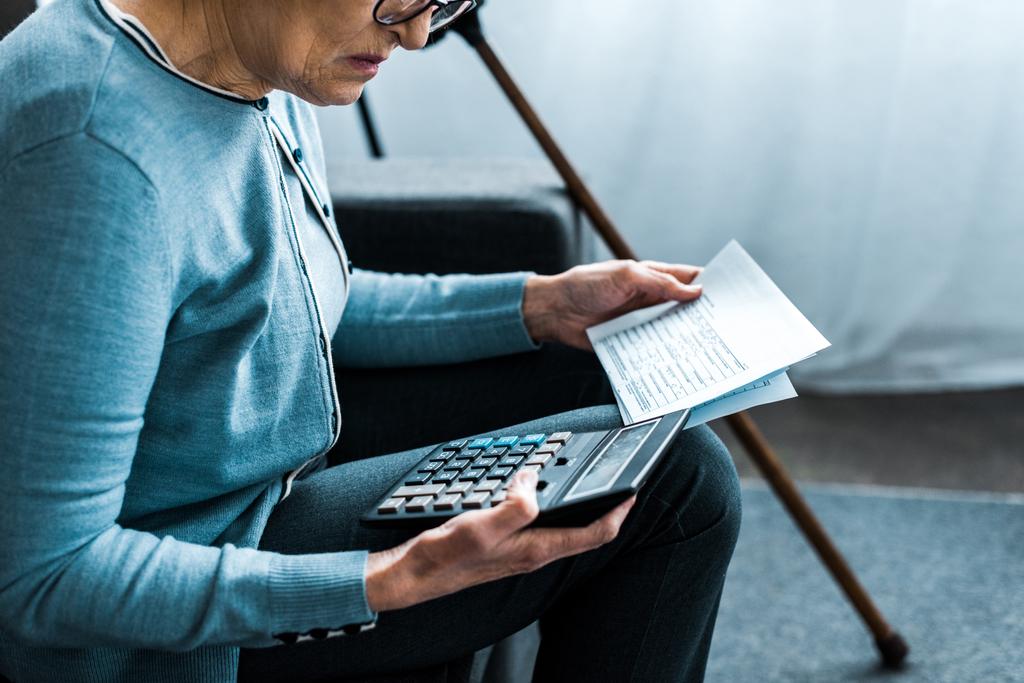 cropped view of senior woman sitting on couch with calculator and counting bills at home - Photo, Image
