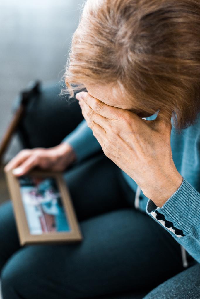 senior woman covering face with hand and crying while looking at picture frame  - Photo, Image