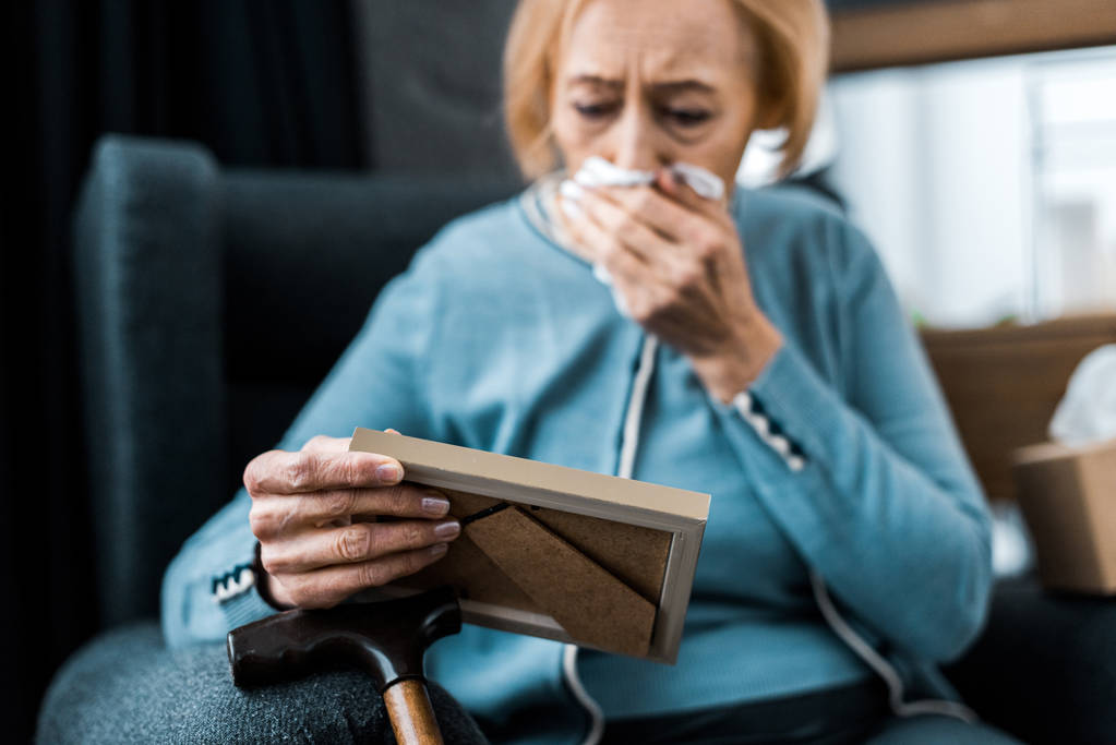 mulher idosa de luto chorando e limpando o rosto de lágrimas com tecido enquanto olha para o quadro de imagem
  - Foto, Imagem