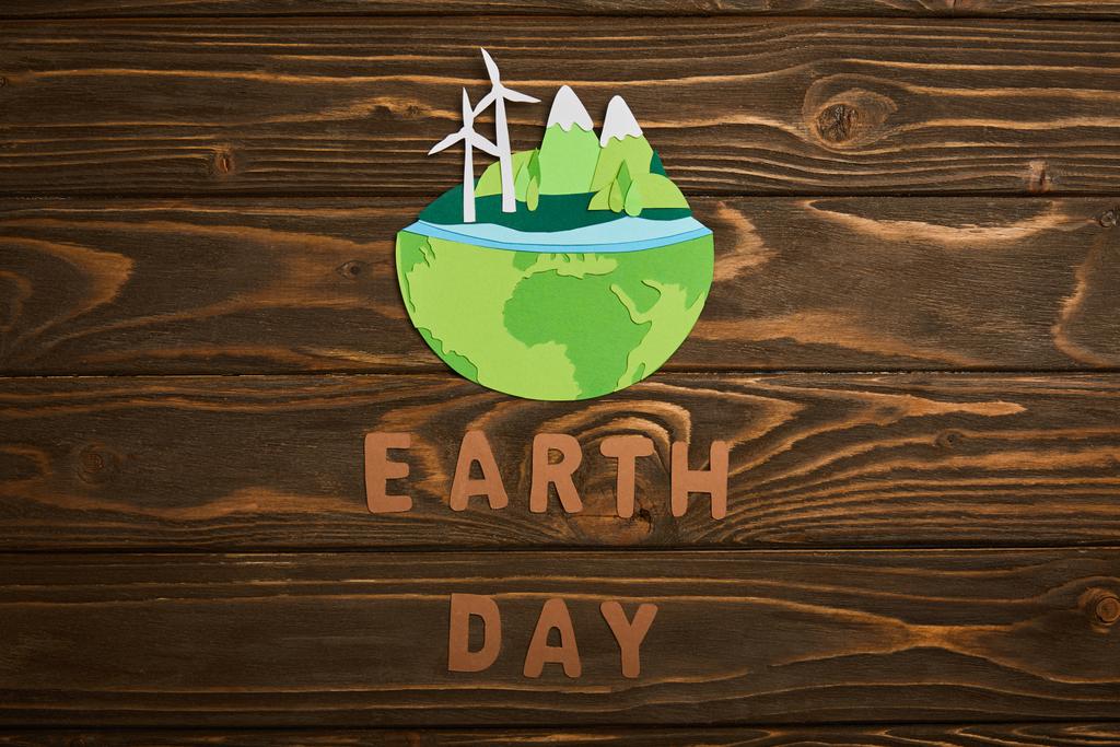 bovenaanzicht van papier knippen planeet met hernieuwbare energiebronnen en/of letters op houten achtergrond, aarde dag concept - Foto, afbeelding