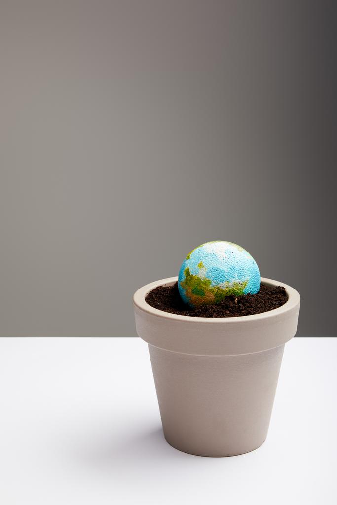 модель планеты помещена в цветочный горшок с почвой на поверхности стола, концепция дня Земли
 - Фото, изображение