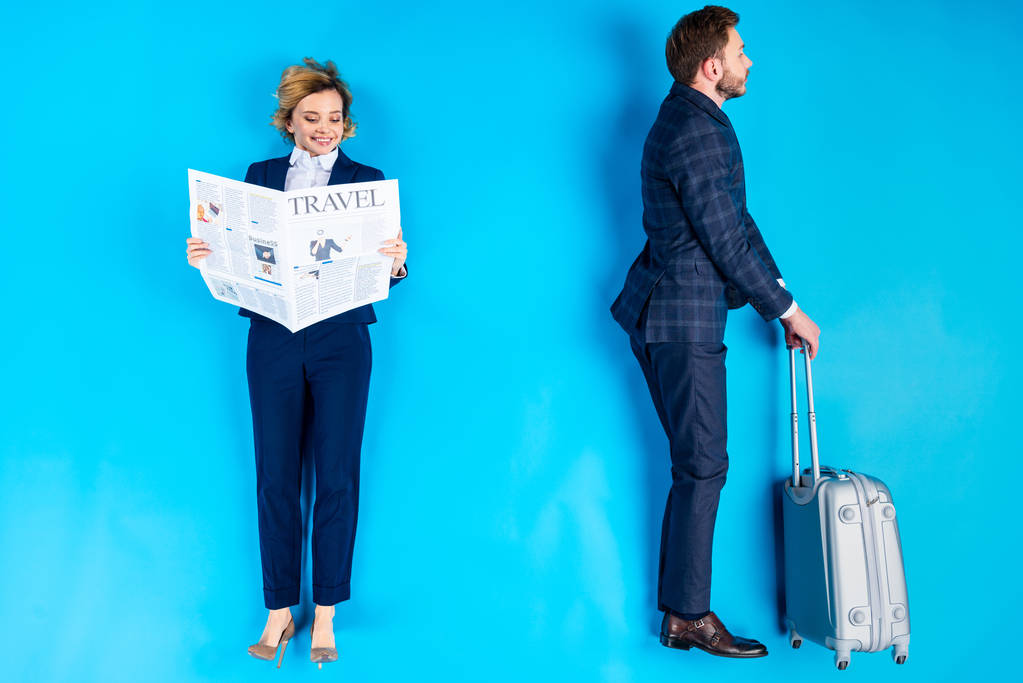 Χαμογελαστή γυναίκα ανάγνωση εφημερίδας ενώ ο άνθρωπος που στέκεται με βαλίτσα σε μπλε φόντο - Φωτογραφία, εικόνα