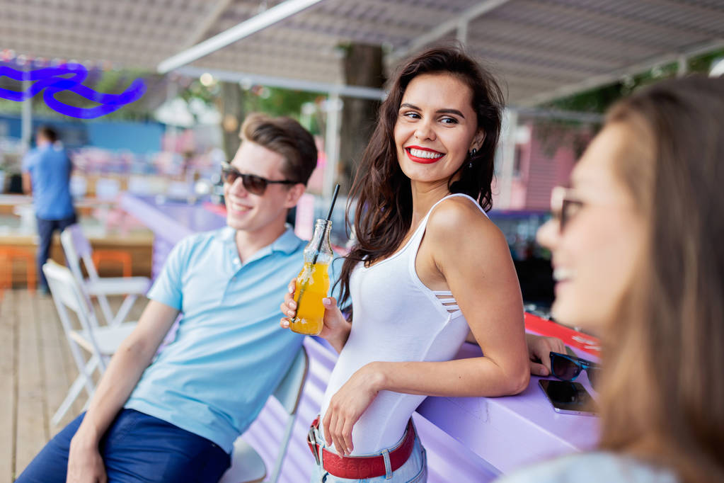 Une compagnie de beaux amis riant, buvant des cocktails jaunes et socialisant au bar dans le joli café d'été. À la tienne. Divertissement, s'amuser. Amitié
. - Photo, image