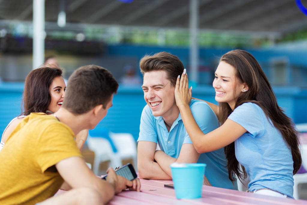 Een gezelschap van knappe vrienden is lachen en zit aan de tafel in het mooie zomerterras. Entertainment, met goede tijd. Vriendschap. - Foto, afbeelding