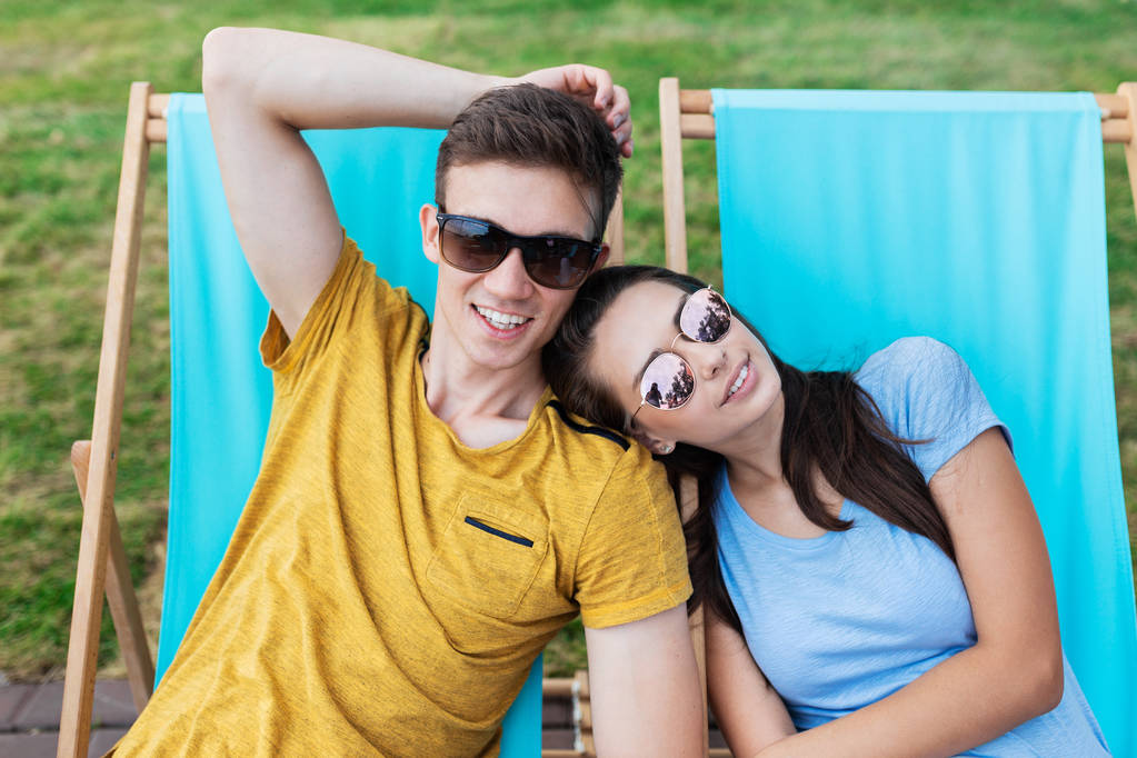 Una hermosa pareja en las gafas de sol está tumbada en las tumbonas en el césped en el agradable café de verano. Entretenimiento, pasándolo bien. Amistad, relación
. - Foto, Imagen