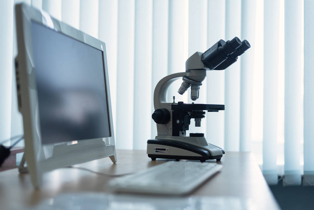 Microscope and a personal computer on a table in a laboratory on a window light background. - Photo, Image