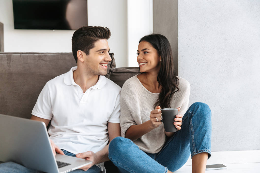 ラップトップ コンピューターを使用して、自宅の床に座って幸せな若いカップル - 写真・画像