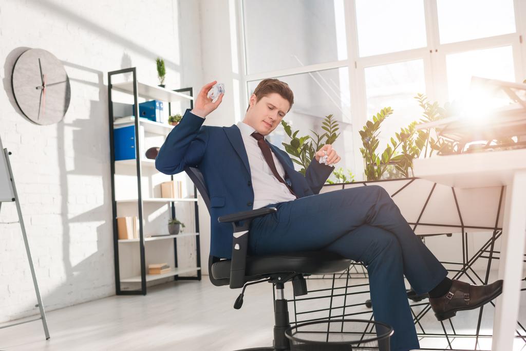 businessman sitting on chair and throwing paper in bin in office, procrastination concept - Photo, Image