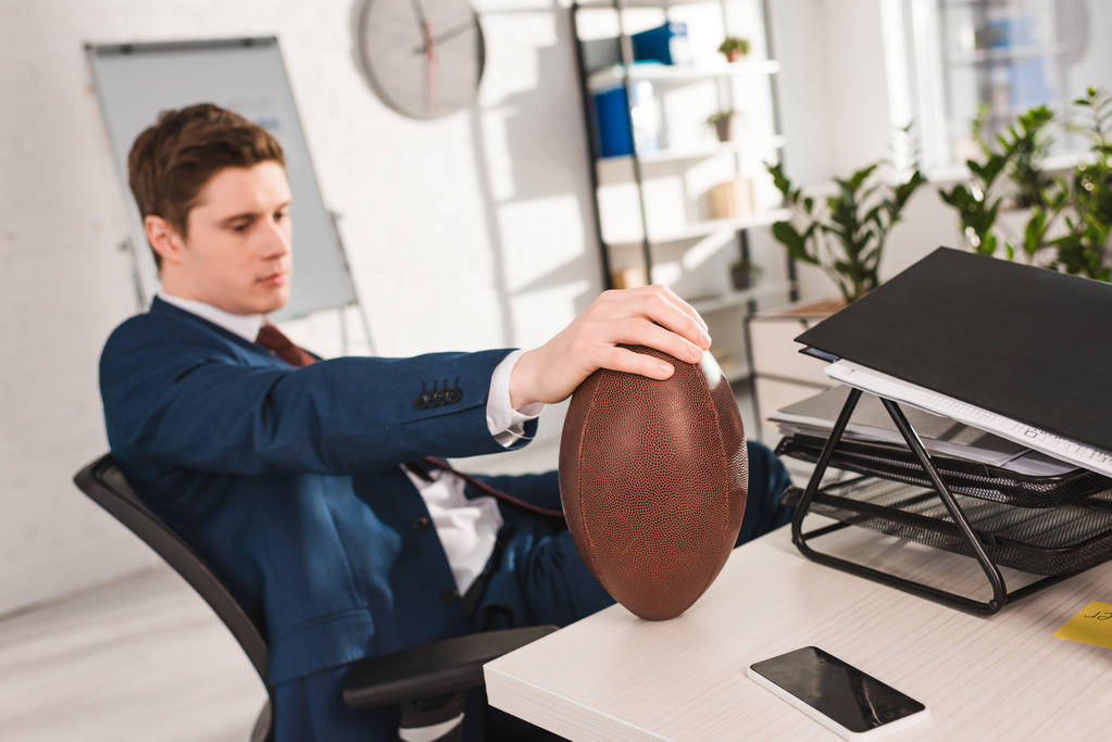 Selektywny fokus rugby piłka w rękach biznesmena w biurze - Zdjęcie, obraz