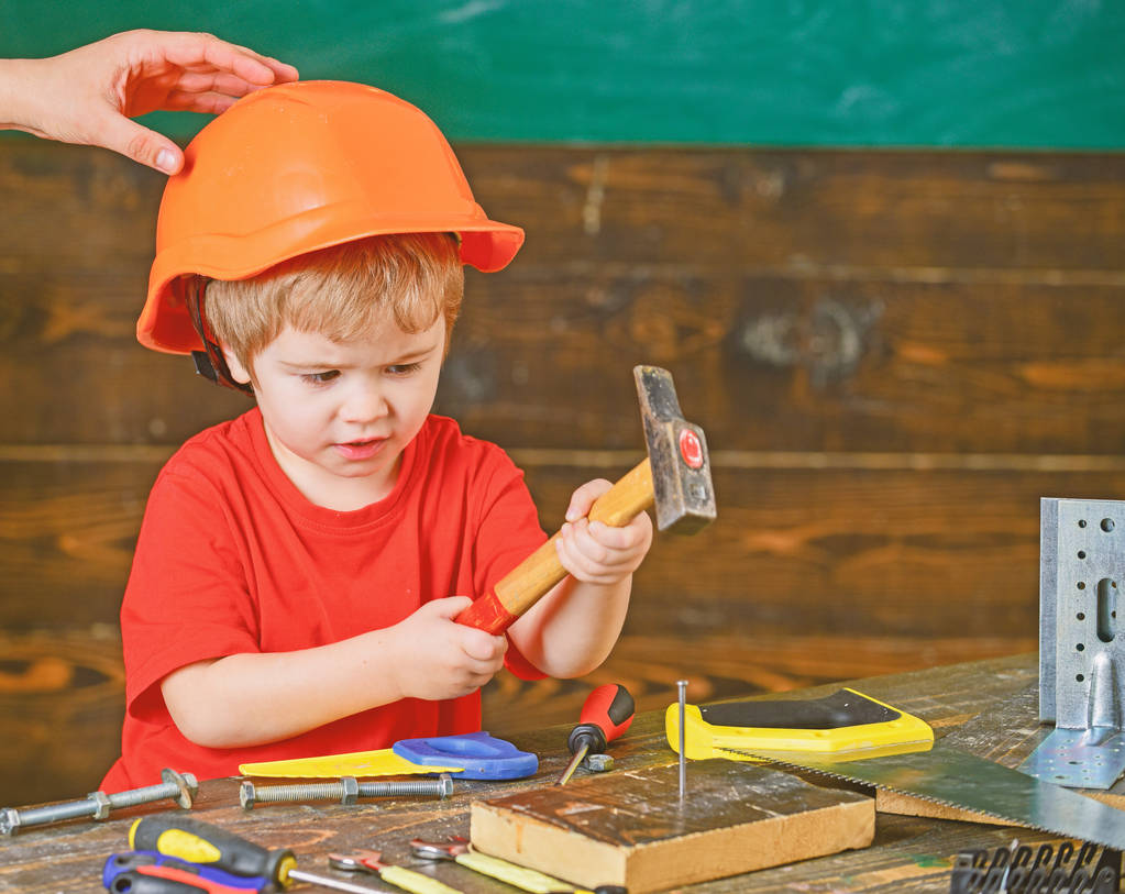 Un chico jugando con un martillo. Papá sosteniendo el sombrero en la cabeza de los hijos. Niño concentrado en taller
 - Foto, imagen