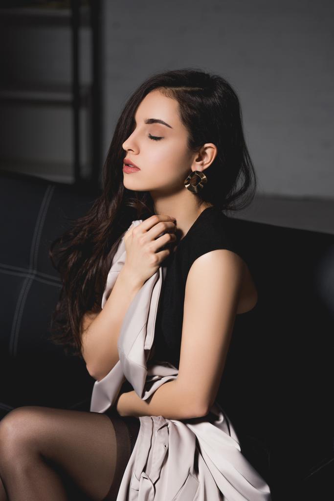 attractive brunette woman in black elegance dress sitting with closed eyes on dark background - Photo, Image