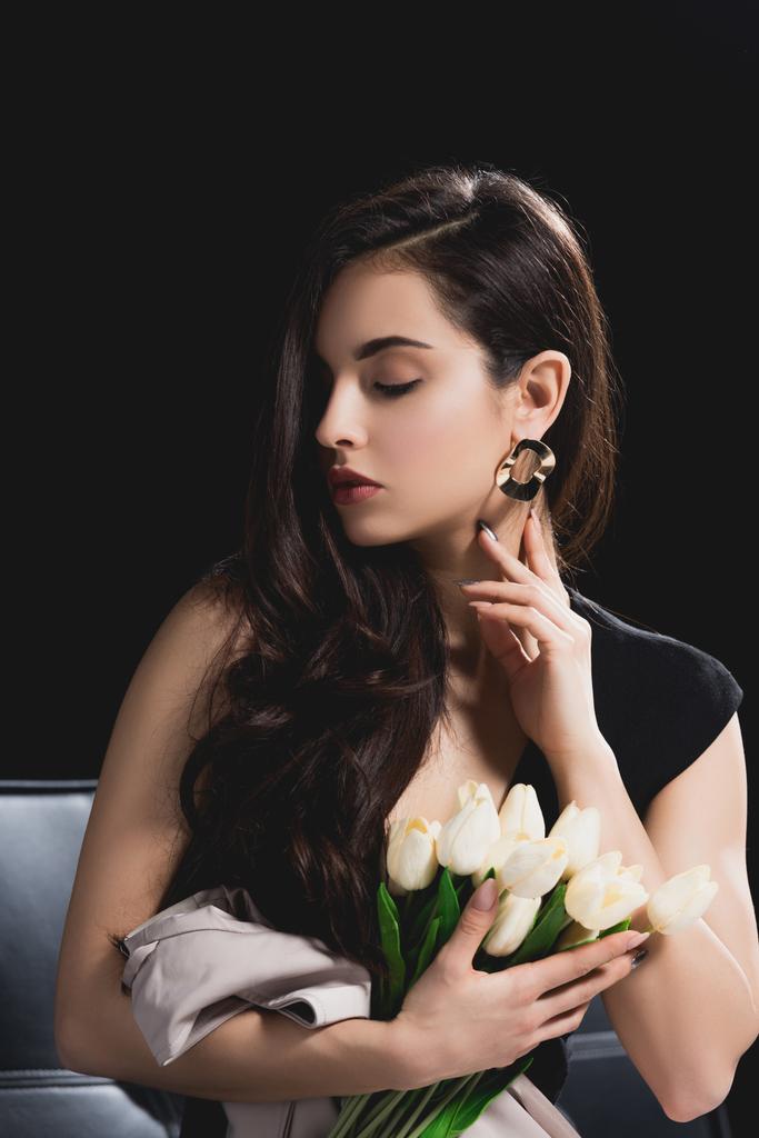 приваблива брюнетка в сукні, що сидить з букетом тюльпанів на чорному фоні
 - Фото, зображення