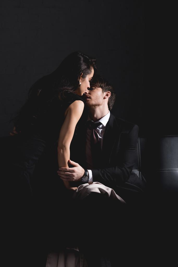 uomo in giacca e cravatta e donna in abito nero baciarsi sul divano su sfondo scuro
 - Foto, immagini