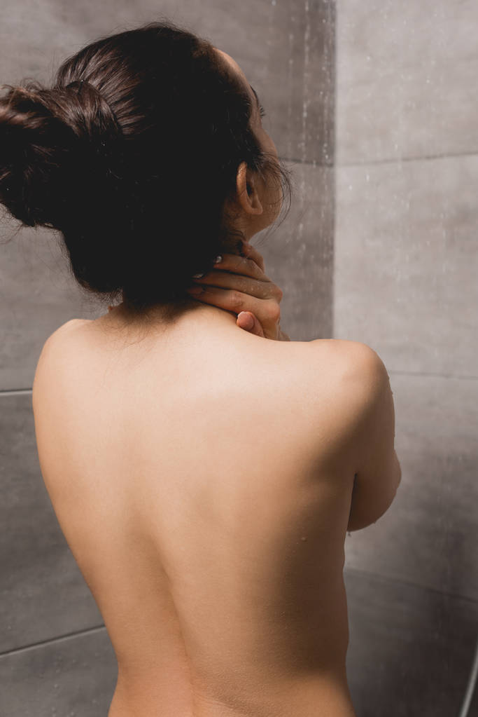 Rückansicht einer nackten Frau unter der Dusche in der Kabine  - Foto, Bild