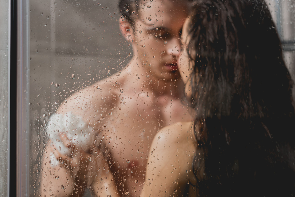 selective focus of man and beautiful woman hugging and taking shower with loofah in cabin  - Photo, Image
