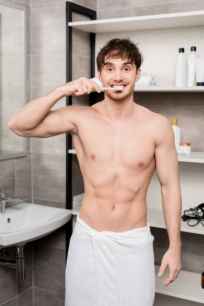 bel homme en serviette brossant les dents et regardant la caméra
  - Photo, image