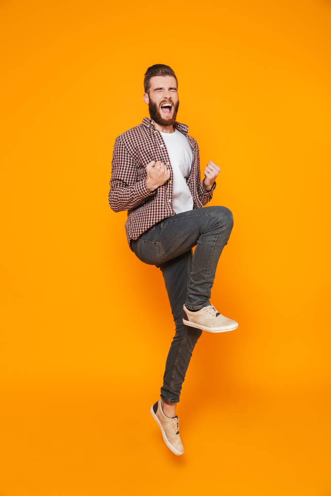 Полный портрет веселого молодого человека в повседневной одежде изолированы на желтом фоне, празднуя успех, прыжок
 - Фото, изображение