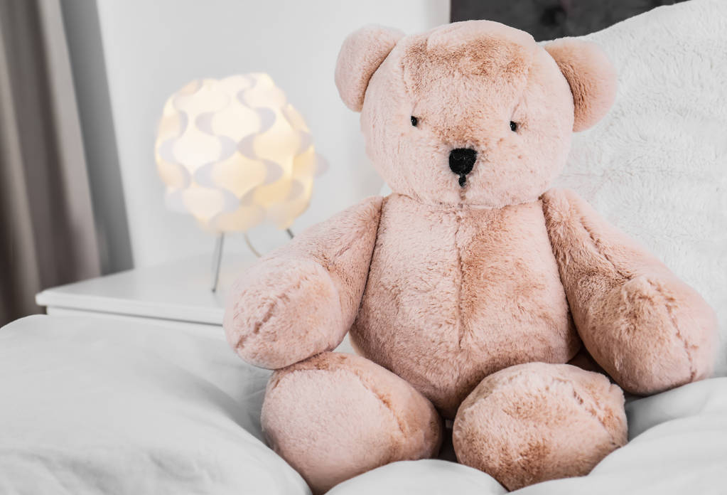 Милий плюшевий ведмідь сидить на ліжку в приміщенні. Простір для тексту
 - Фото, зображення