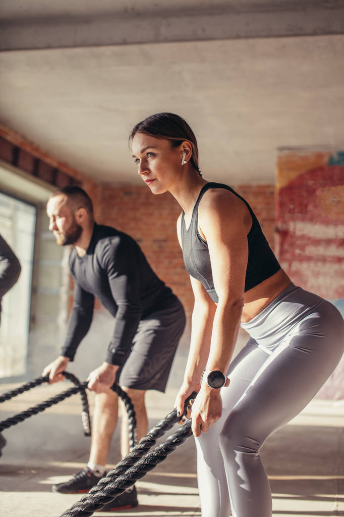 Γυναίκα και άντρας στο γυμναστήριο λειτουργική προπόνηση με μάχη σχοινί άσκηση - Φωτογραφία, εικόνα