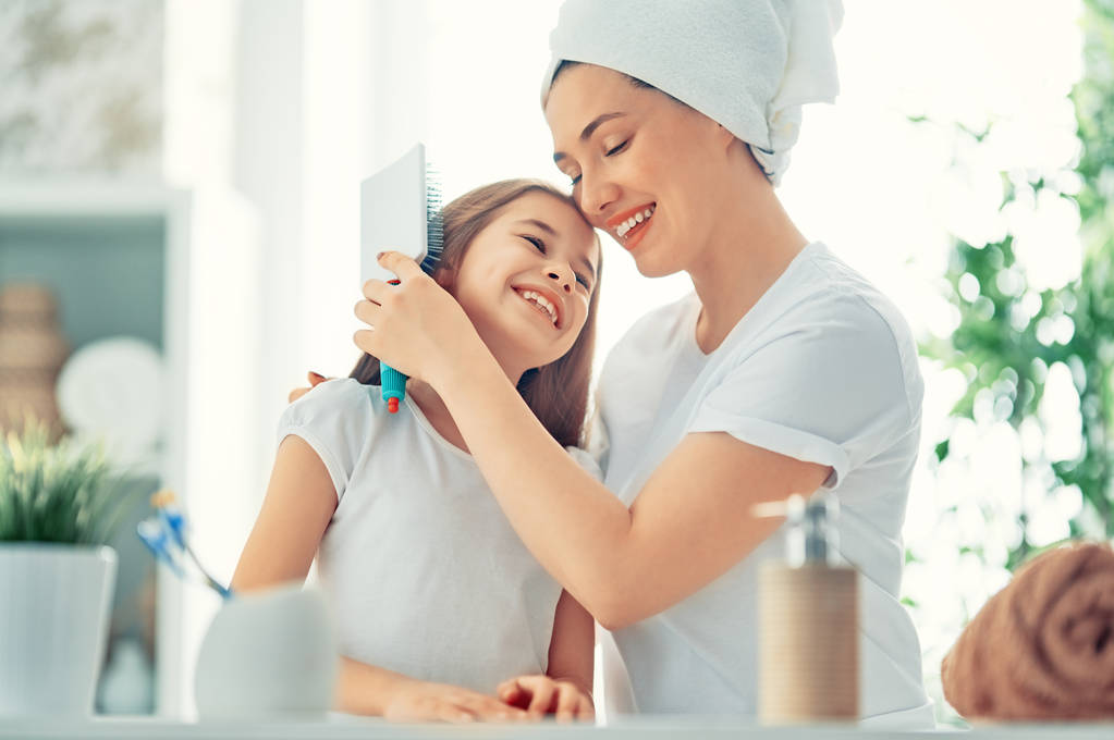 Famiglia felice! Madre e figlia bambina stanno pettinando i capelli in bagno
. - Foto, immagini