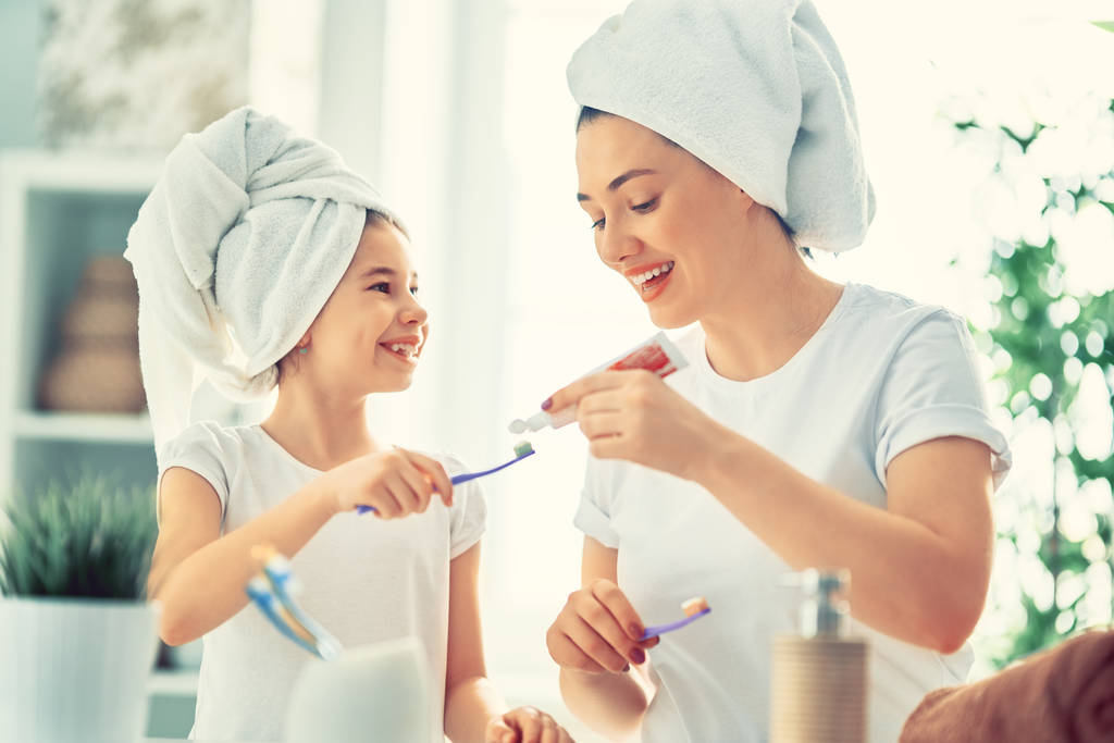 Счастливая семья! Мать и дочь девочка чистят зубы зубными щетками в ванной комнате
. - Фото, изображение
