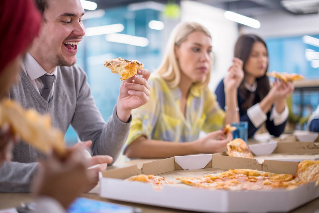 Przyjazny różnorodny wieloetniczny zespół biznesowy jedzący razem pizzę w biurze startupów, wielorasowa grupa pracowników ciesząca się przerwą w rozmowie śmiejąc się w porze lunchu na spotkaniu - Zdjęcie, obraz
