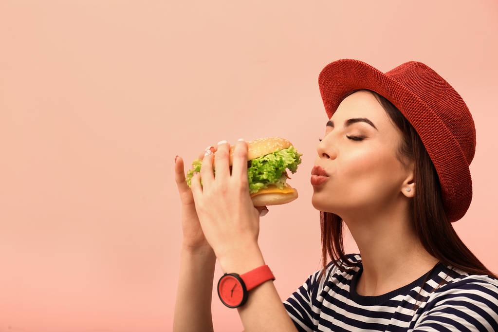 Young woman eating tasty burger on color background. Space for text - Photo, Image