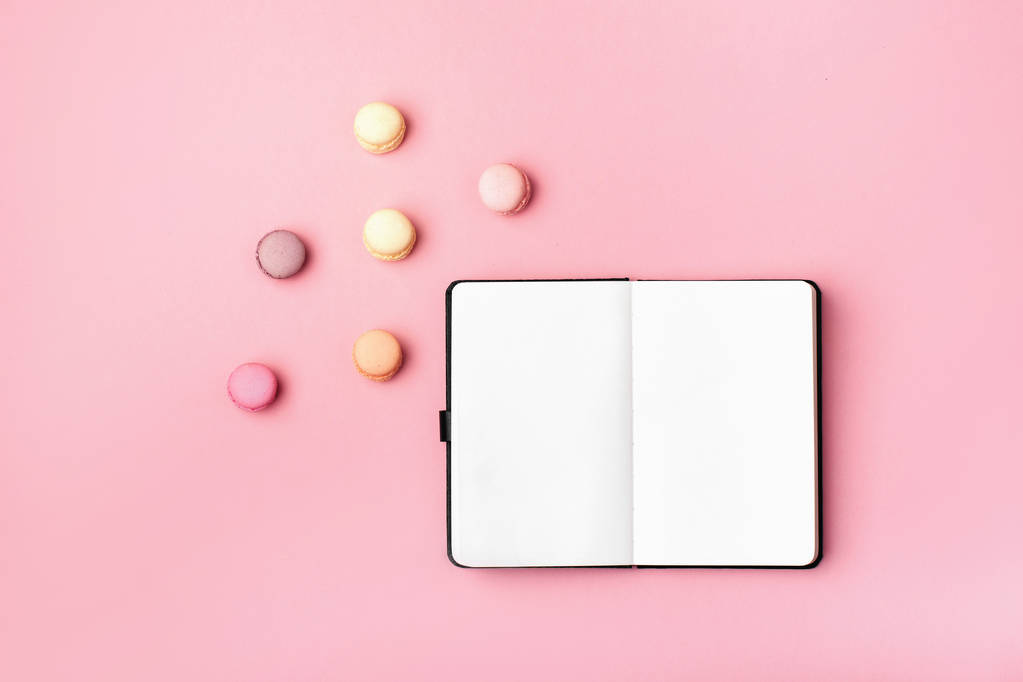 Notebook and colorful macaron on pastel pink desk top view. - Photo, Image