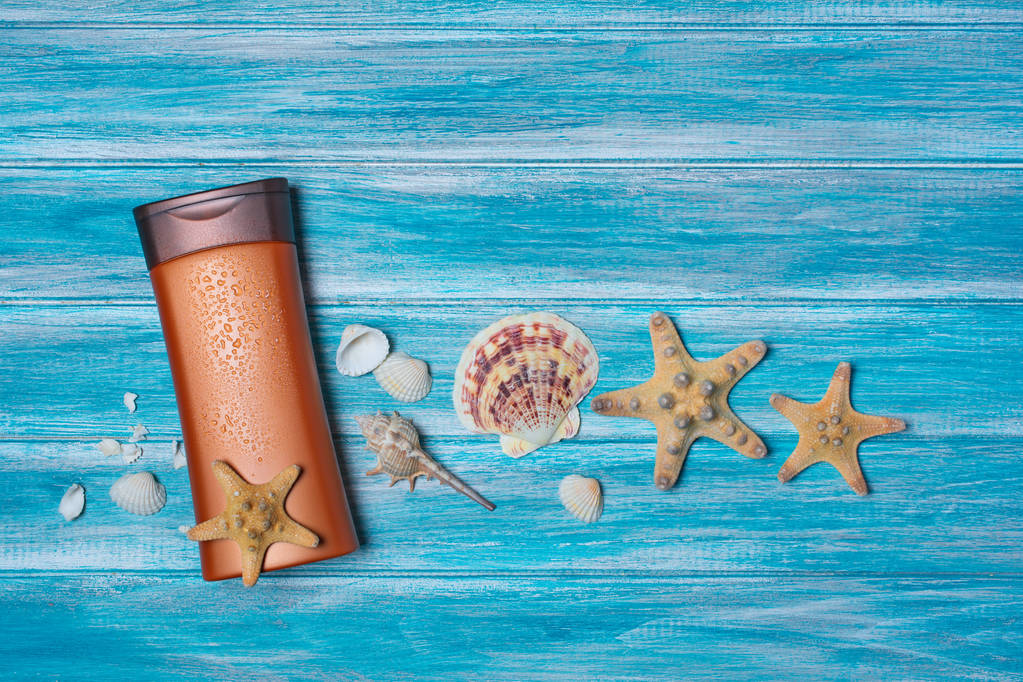 Bovenaanzicht op bronzen fles met zonnebrandcrème en schelpen als concept vakantie tijd op blauwe houten achtergrond - Foto, afbeelding