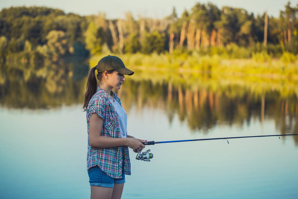 Cute woman is fishing with rod on the summer lake - Photo, Image