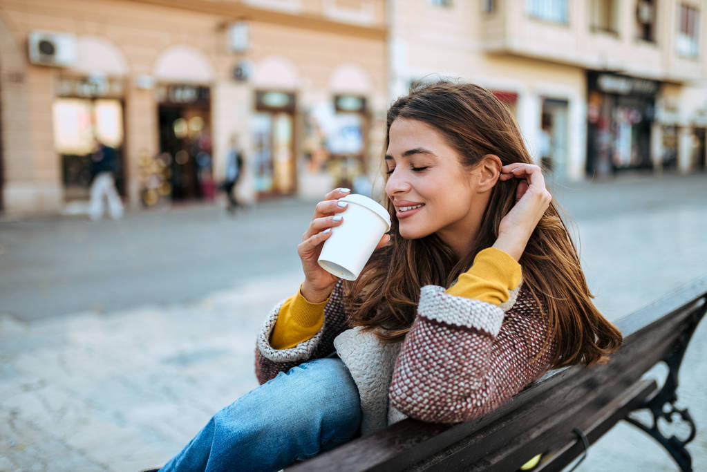 街のベンチに座ってコーヒーを飲みながら美しいブルネット. - 写真・画像