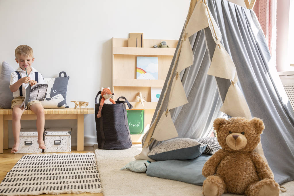 Teddy bear next to grey scandinavian tent in stylish boy's bedroom with furniture made from natural materials, real photo with copy space on the white wall - Photo, Image