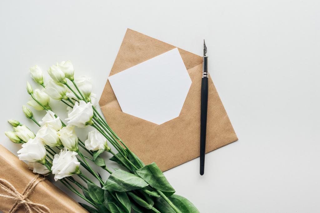 Draufsicht auf Eustoma, verpacktes Geschenk, Umschlag mit leerer Karte und Tintenstift auf grauem Hintergrund  - Foto, Bild