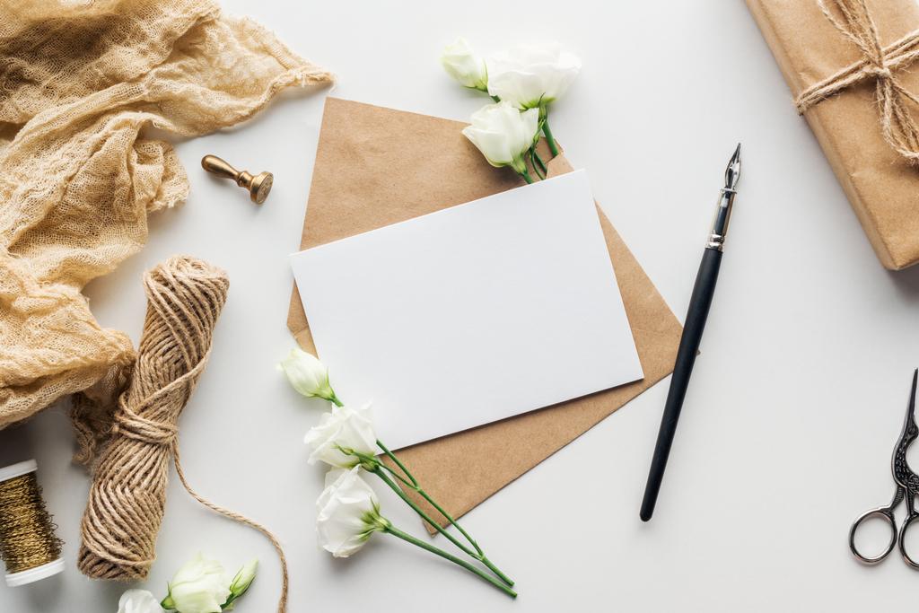 Draufsicht auf Blumen, Stoff, Briefmarke, Umschlag mit leerer Karte und Tuschstift auf grauem Hintergrund - Foto, Bild