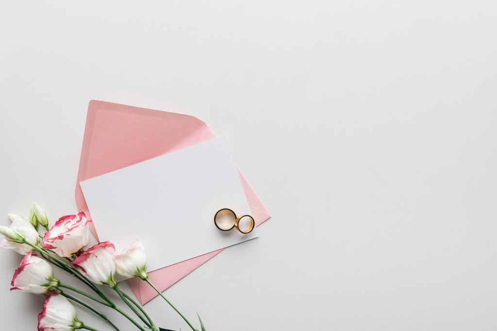 κάτοψη του κενή κάρτα με ροζ φάκελο, eustoma και Χρυσές βέρες σε γκρίζο φόντο - Φωτογραφία, εικόνα