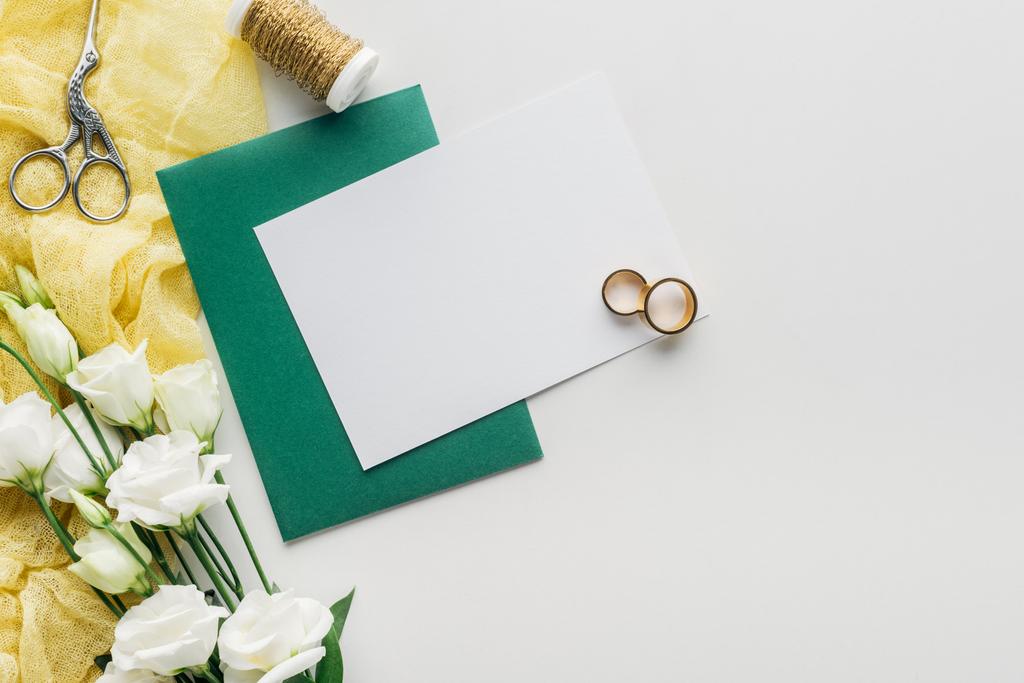 灰色の背景に緑の封筒、花、布、糸、はさみ、黄金の結婚指輪のスプールと空カードのトップ ビュー - 写真・画像