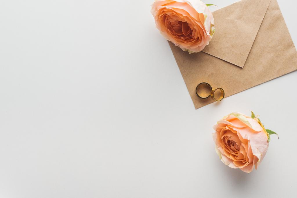 Draufsicht auf braunes Bastelpapier-Umschlag, Blumen und goldene Eheringe auf grauem Hintergrund - Foto, Bild