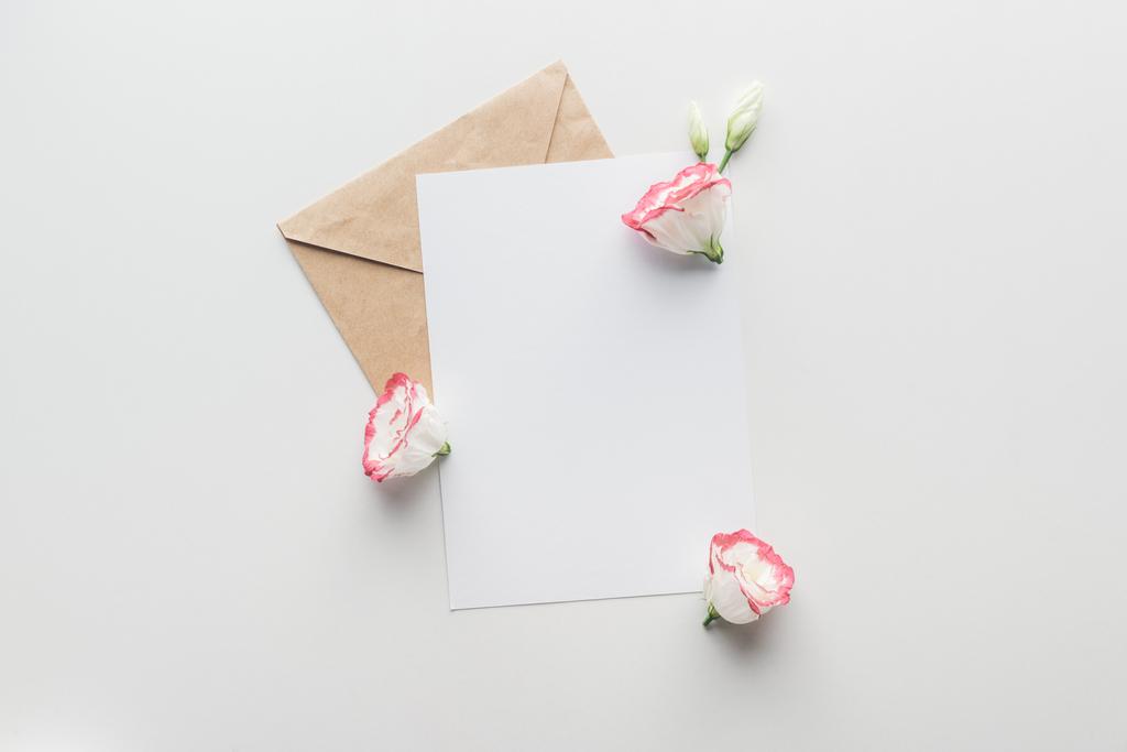 Draufsicht auf leeren Rohling mit braunem Bastelpapier-Umschlag und Eustoma auf grauem Hintergrund - Foto, Bild