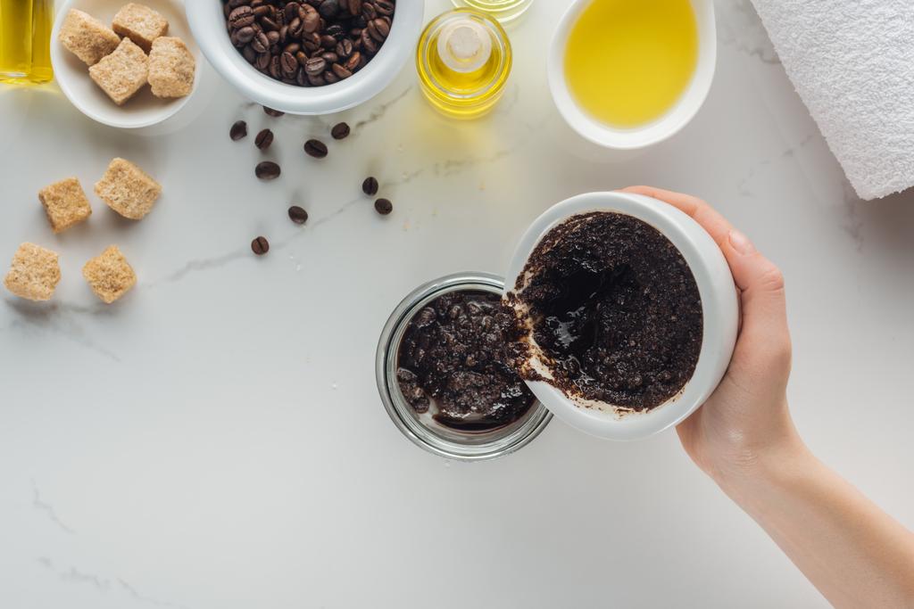 cropped view of  woman pouring homemade coffee scrub into glass container on white surface - Photo, Image