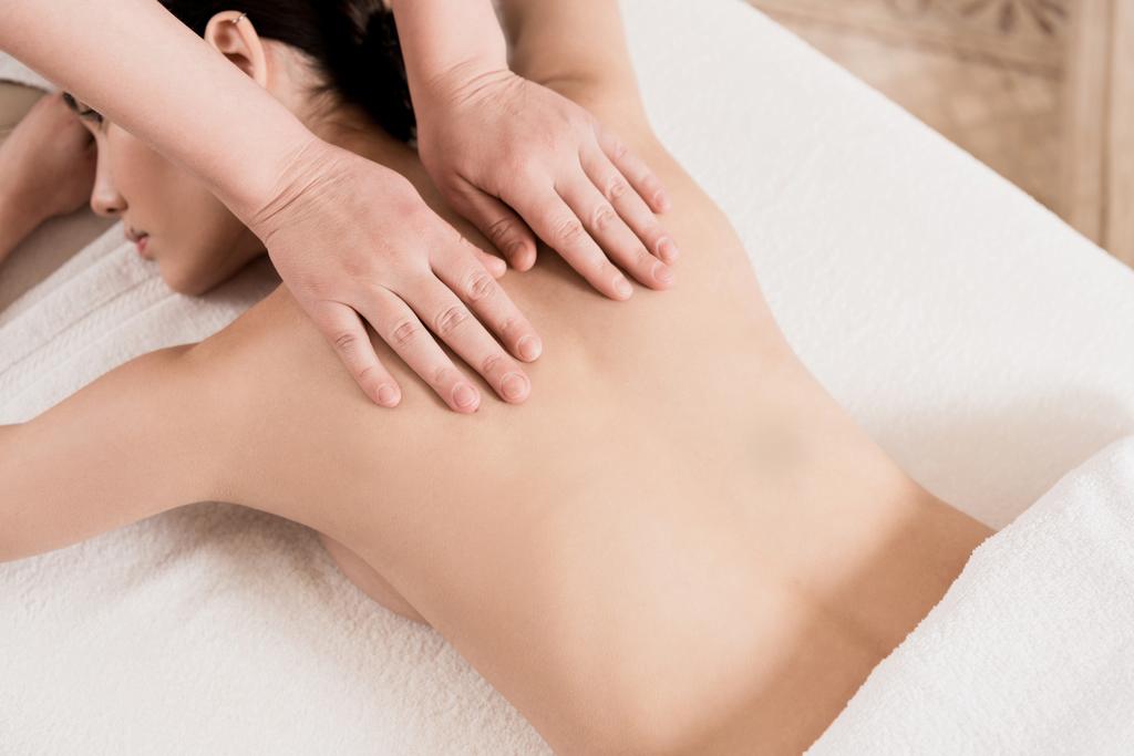 bijgesneden weergave van masseur doet rugmassage om aantrekkelijke vrouw  - Foto, afbeelding