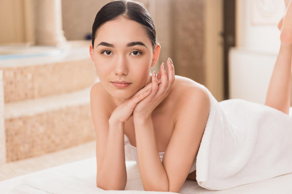 krásná asijská žena v ručníku lhaní a při pohledu na fotoaparát  - Fotografie, Obrázek