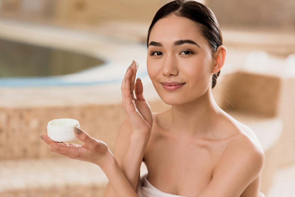 schöne asiatische Frau Anwendung kosmetischer Creme und Blick auf die Kamera  - Foto, Bild