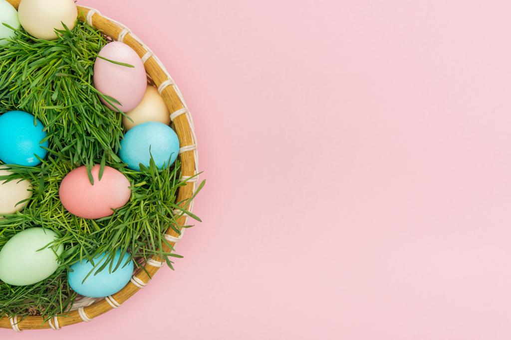 vista superior de los huevos de Pascua en plato de mimbre con césped aislado en rosa con espacio de copia
 - Foto, Imagen