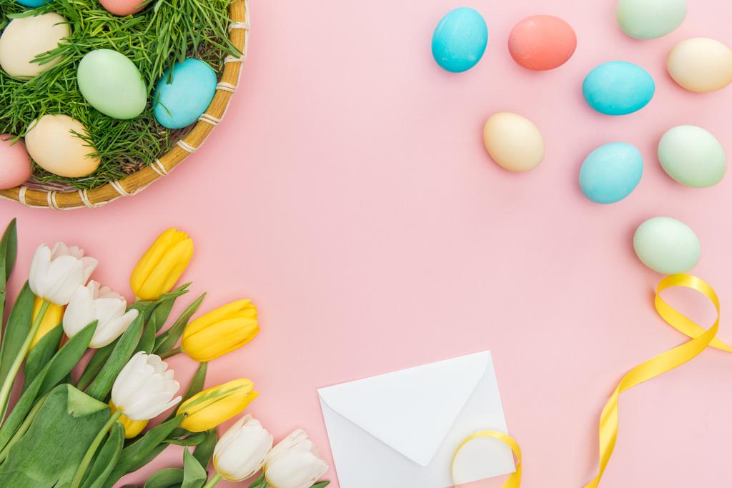 vue du dessus des œufs de Pâques dans une assiette en osier, des tulipes et une enveloppe isolées sur rose
 - Photo, image