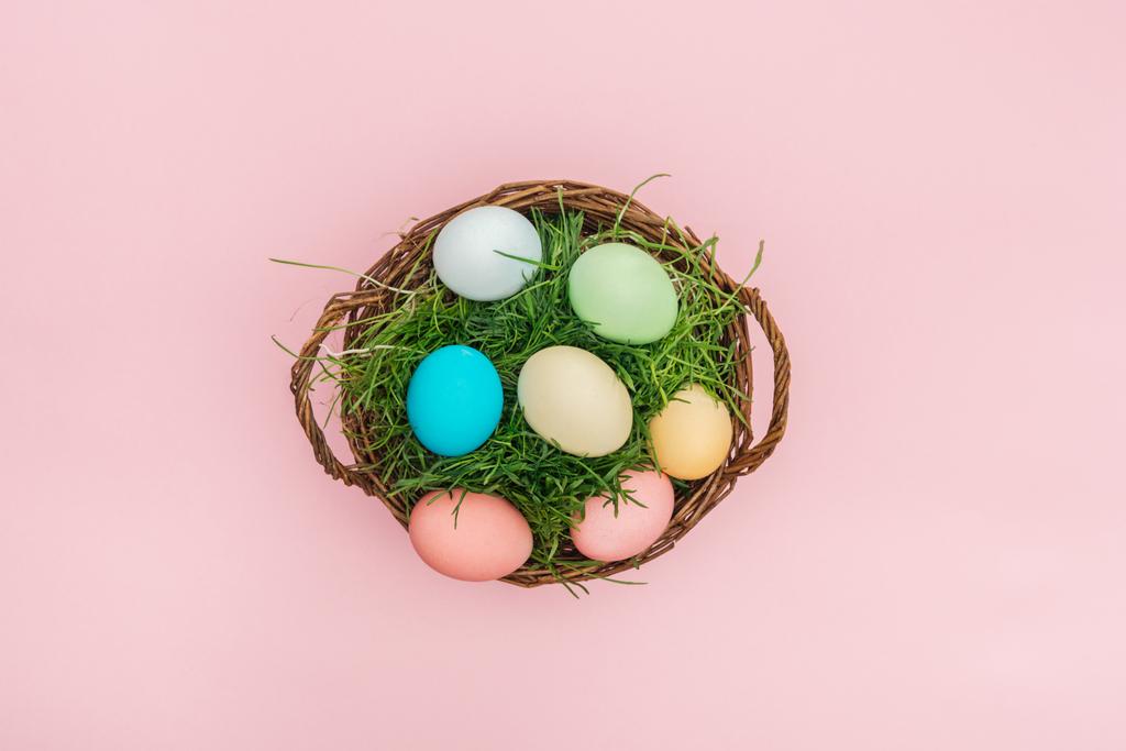 top view of easter eggs in wicker basket with grass isolated on pink - Photo, Image