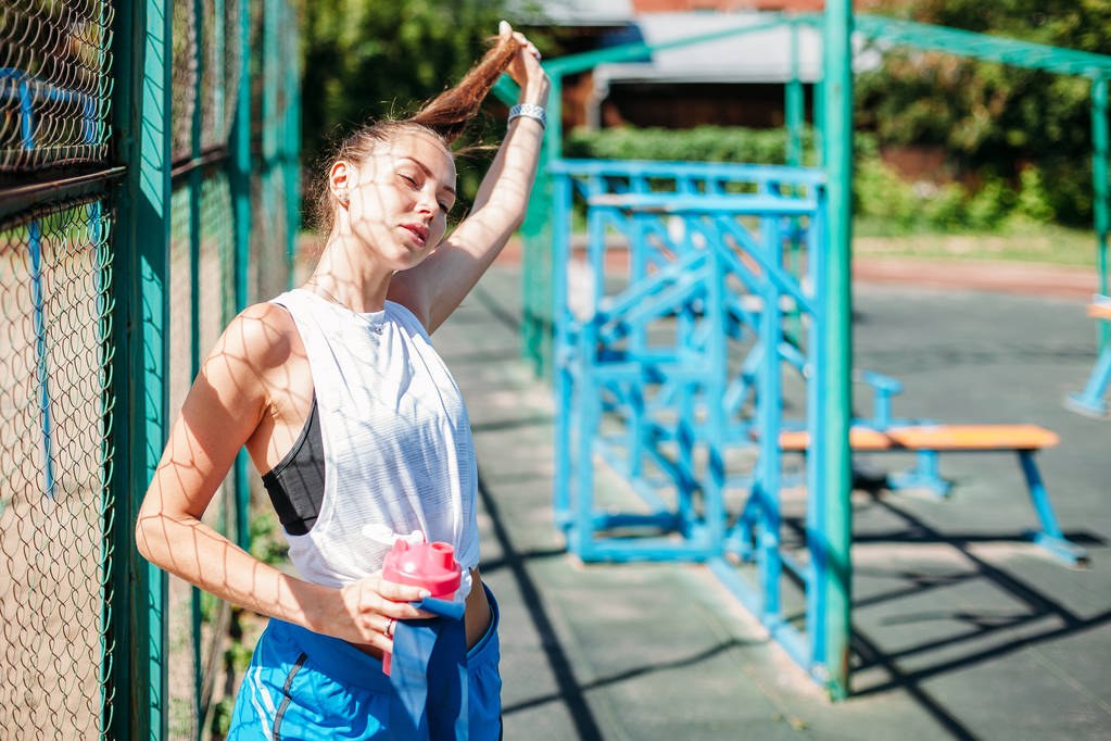 sportos fiatal nő, egy üveg víz pózol az atlétikai pálya - Fotó, kép